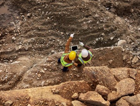 Top view shot of two industrial  workers wearing reflective jackets standing on mining worksite outdoors using digital tablet, copy space